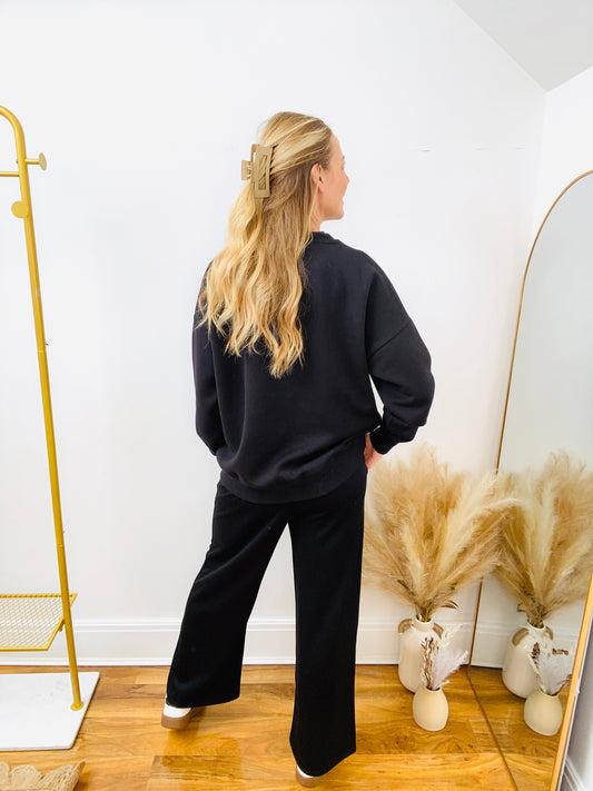 Back view woman wearing a black sweatshirt and black joggers and trainers.