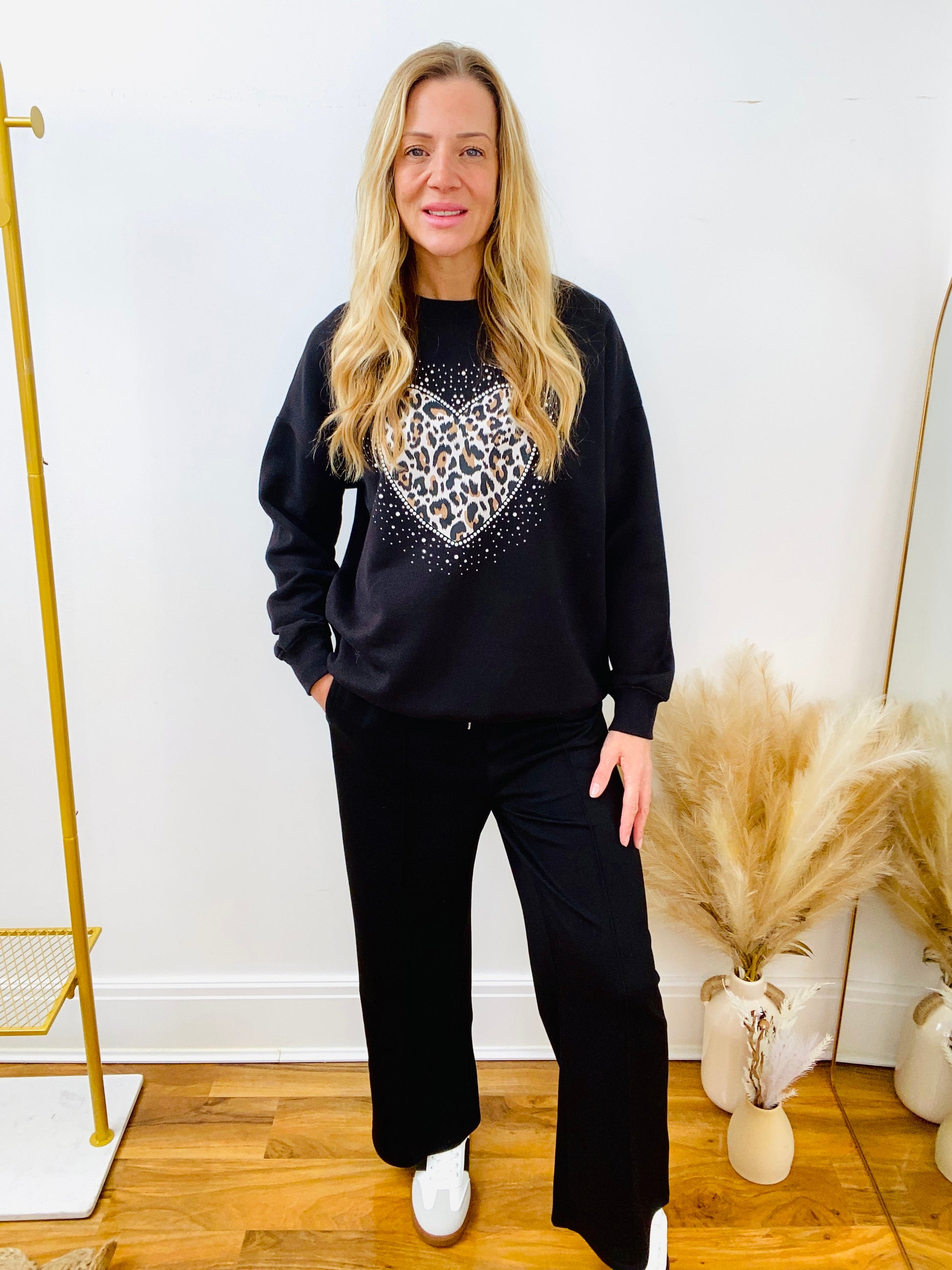 Woman wearing a black sweatshirt with leopard love heart and black joggers and trainers.